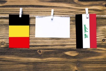 Hanging flags of Belgium and Iraq attached to rope with clothes pins with copy space on white note...