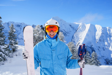 Portrait of happy sporty man in helmet and mountain skis against background of mountains in afternoon