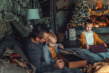 Dad plays with his son in the New Year at the Christmas tree and fireplace.