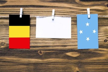 Hanging flags of Belgium and Micronesia attached to rope with clothes pins with copy space on white note paper on wooden background.Diplomatic relations between countries.