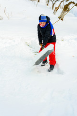 The boy shovels the snow near his house in winter.