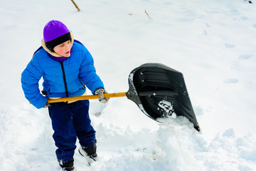 Smiling boy is carrying snow on a shovel, Child cleans the yard after a snowfall.