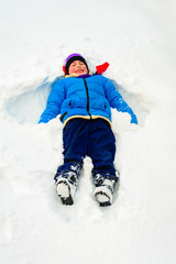 Fototapeta na wymiar A boy in white fluffy snow makes an angel.