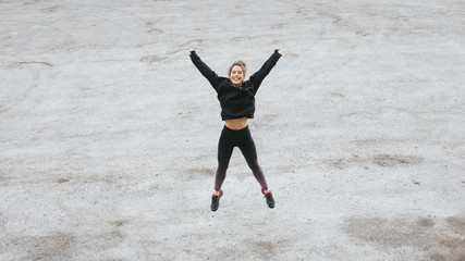 Obraz premium Fitness lifestyle and workout success concept. Happy woman jumping and raising arms on a road. Runner celebrating training goals.