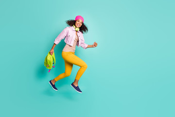 Full length body size side profile photo of casual positive jumping running school girl aspiring to come to educational complex on time in yellow pants pink jacket t-shirt isolated vivid color teal