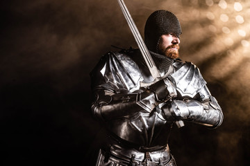 handsome knight in armor holding sword on black background