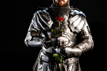 cropped view of knight in armor holding rose isolated on black