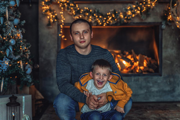 Dad plays with his son in the New Year at the Christmas tree and fireplace.