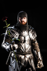 Fototapeta na wymiar handsome knight in armor holding rose isolated on black