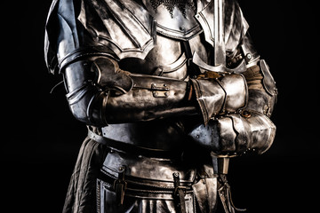 cropped view of knight in armor holding sword isolated on black - obrazy, fototapety, plakaty