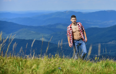Naklejka premium Muscular tourist walk mountain hill. Hiker muscular torso reach mountain peak. Athlete guy relax mountains. Beautiful environment. Hiking concept. Man stand top mountain landscape background