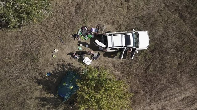 Camera accends over the wild campers with white car and reveals landscape with trees, road and river