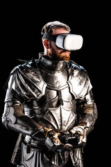 KYIV, UKRAINE - OCTOBER 9, 2019: knight with virtual reality headset in armor holding joystick on black background