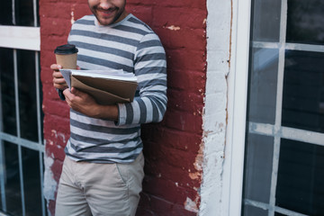 cropped view of smiling businessman holding documents and coffee to go