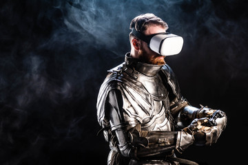 Naklejka premium KYIV, UKRAINE - OCTOBER 9, 2019: knight with virtual reality headset in armor holding joystick on black background