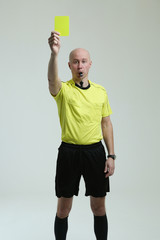 bald football referee on white background. the referee shows a yellow card and looks into the...