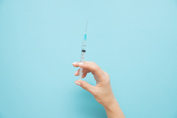 Beauty spa doctor holding syringe on blue background. Female hand with manicure