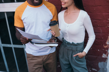 cropped view of african american businessman showing documents to colleague holding coffee to go