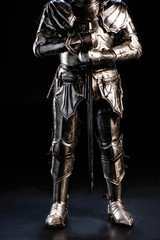 cropped view of knight in armor holding sword on black background