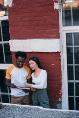 smiling african american businessman showing documents to attractive colleague holding coffee to go