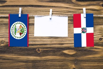 Hanging flags of Belize and Dominican Republic attached to rope with clothes pins with copy space on white note paper on wooden background.Diplomatic relations between countries.