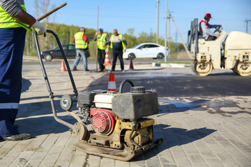 asphalt paving works at summer. vibrating plate compactor on the road