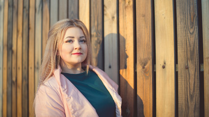 A portrait of a beautiful girl, posing near a wooden fence at sunset in springtime.