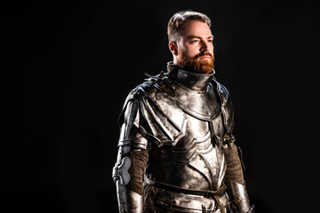 Fototapeta na wymiar handsome knight in armor looking away isolated on black