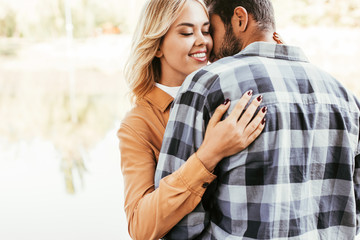 Fototapeta premium happy young woman embracing boyfriend while standing near lake in park