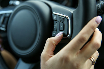woman's hand presses the button on the steering wheel of the car close-up