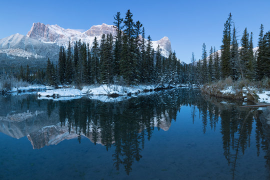 Almost nearly perfect reflection of the Three Sisters Peaks in the Bow River. Near Canmore, Alberta Canada. Winter season is coming. Bear country. Beautiful landscape background concept.