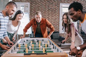 excited multicultural businesspeople playing table football in office
