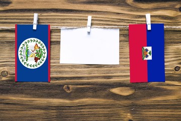 Hanging flags of Belize and Haiti attached to rope with clothes pins with copy space on white note paper on wooden background.Diplomatic relations between countries.