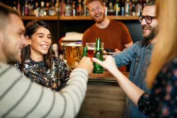Friends standing in bar and toasting with beer.