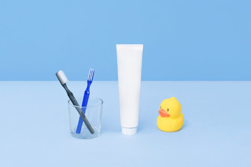 Toothbrushes and tube of toothpaste with rubber yellow duck on blue background. Teeth hygiene concept. Flat lay. Natural beauty products for branding mockup concept. Add your text.