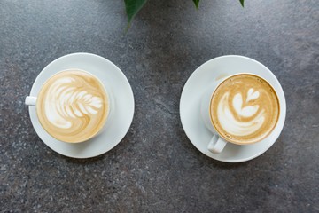 Two white cups of coffee art on gray stone countertop