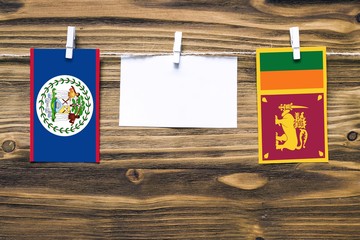 Hanging flags of Belize and Sri Lanka attached to rope with clothes pins with copy space on white note paper on wooden background.Diplomatic relations between countries.