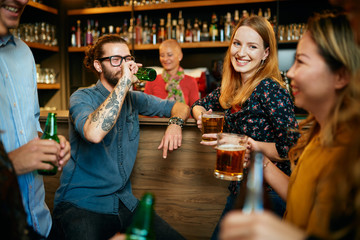 Group of friends drinking beer, chatting and having good time at pub. Night out.