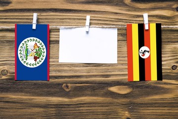 Hanging flags of Belize and Uganda attached to rope with clothes pins with copy space on white note paper on wooden background.Diplomatic relations between countries.