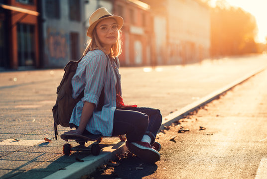 Portrait of smiling girl sitting on long board in the city during sunset.