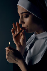 Close-up portrait of a nun, taking on a black background. She wearing dark nun's clothing. The nun...