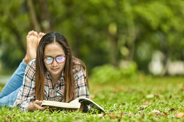 .Woman spend the holidays relaxing, reading books in the garden with trees and green grass. On a bright day