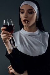 Cropped shot of a nun, posing on a black background. She's wearing dark nun's clothing. The nun is...