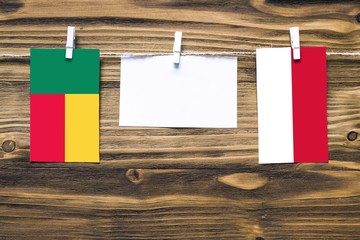 Hanging flags of Benin and Indonesia attached to rope with clothes pins with copy space on white note paper on wooden background.Diplomatic relations between countries.