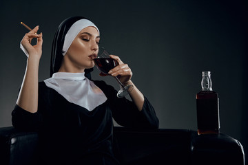 Cropped half-turn shot of a nun, sitting on a chair. She's wearing dark nun's clothing. The nun is...