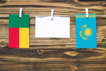 Hanging flags of Benin and Kazakhstan attached to rope with clothes pins with copy space on white note paper on wooden background.Diplomatic relations between countries.