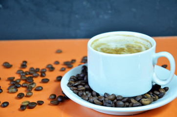 warm cup of coffee cappuccino with cream in a white cup on an orange and black background with coffee beans with a teaspoon