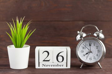 November 26 on a wooden calendar next to an alarm clock on a wooden background, the calendar date of the last autumn month