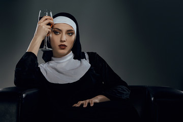 Cropped shot of a nun, sitting on a chair. She's wearing dark nun's clothing. The nun is looking to...