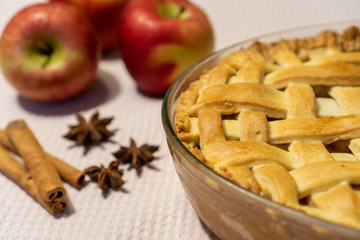 Closeup of a freshly baked apple pie in an autumn decor, on a table decorated with spices, cinnamon and star anise, and red apples.